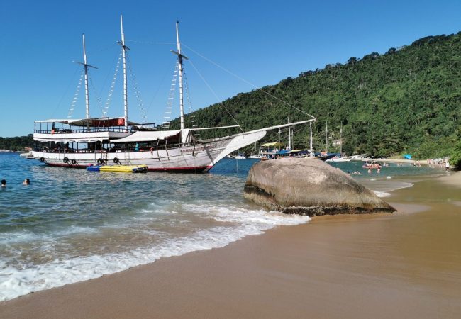 Дървен ветроход край плажовете на Иля Гранде – кристални води и зелени хълмове на бразилското крайбрежие.